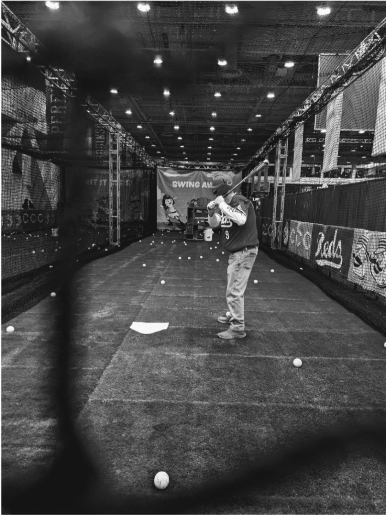 black and white photo of man in a batting cage with a helmet